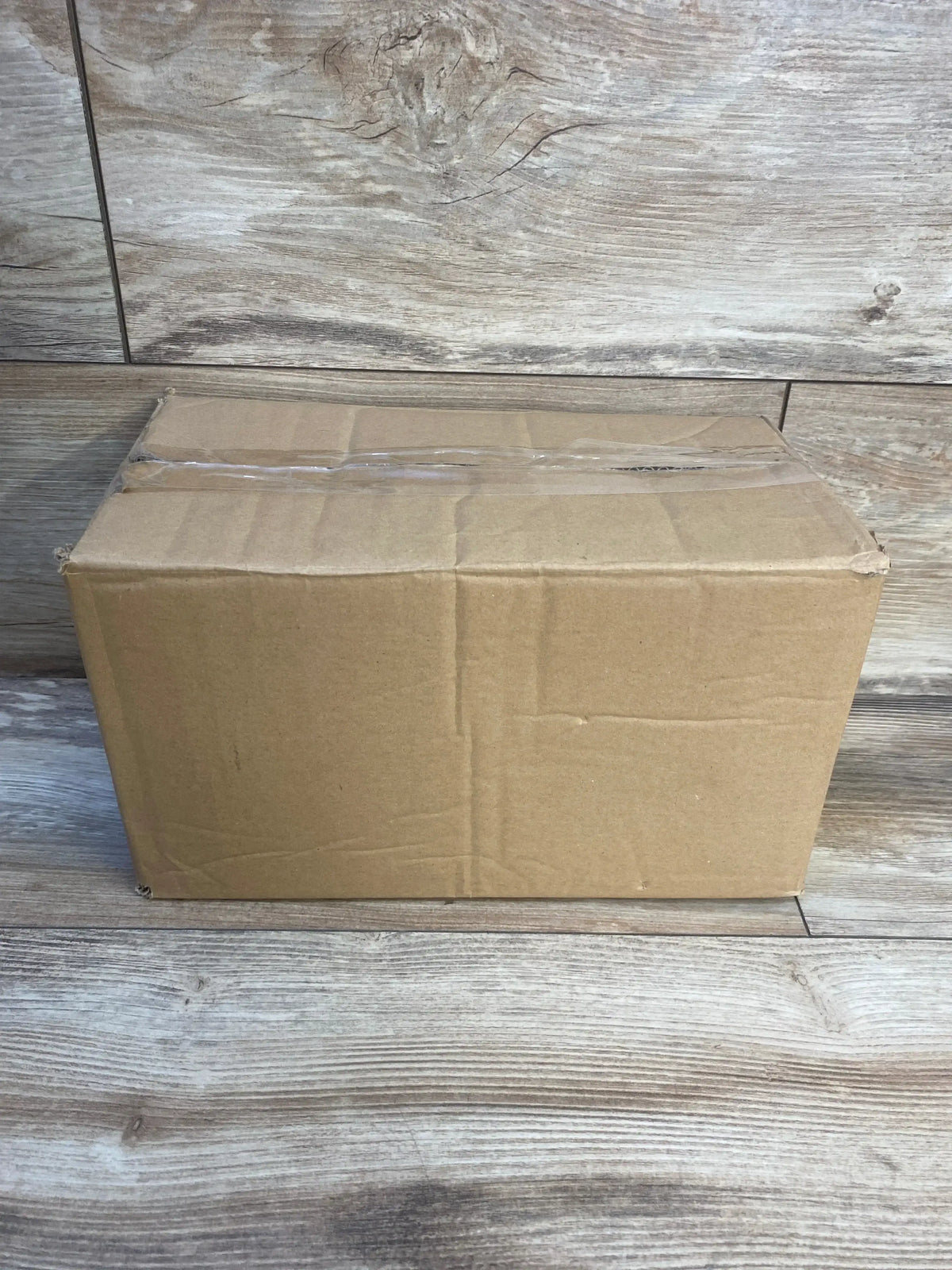 Front view of LuQiBabe travel potty kit 4pc packaged in a sealed kraft shipping box on wood plank floor