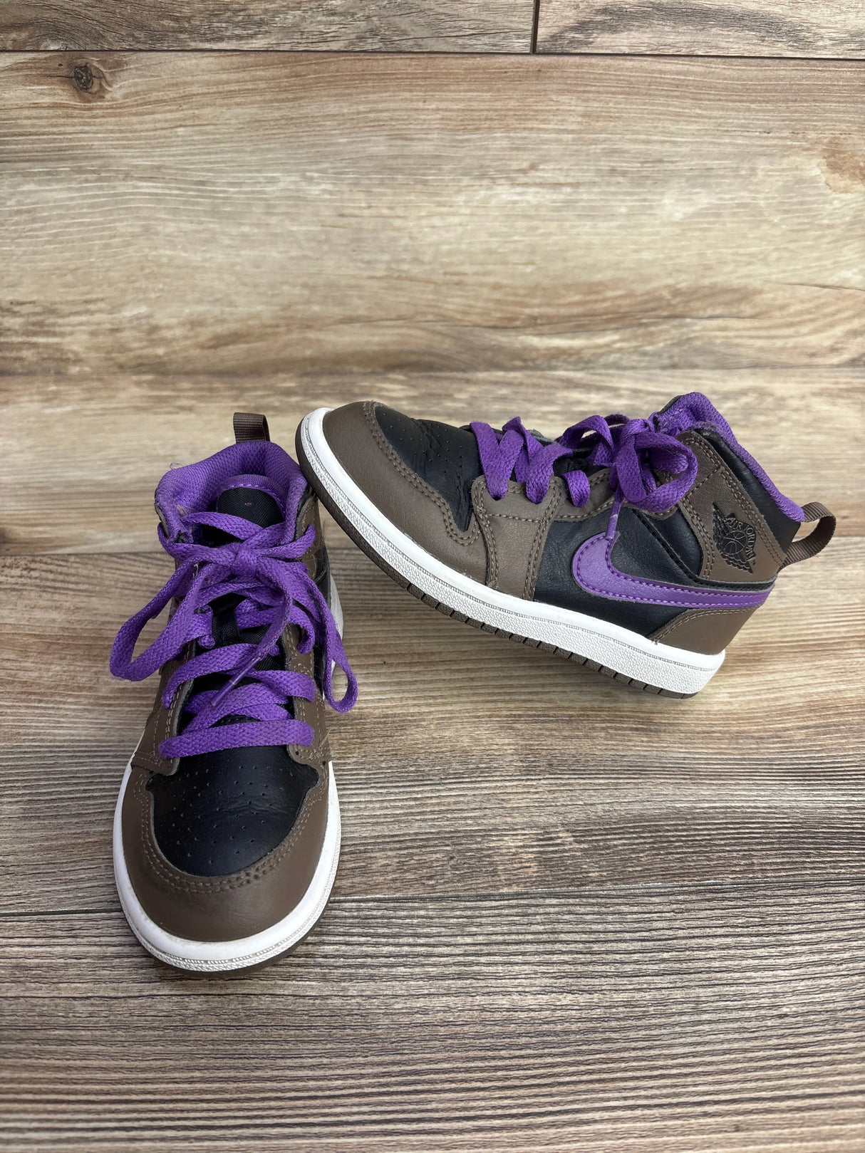 Children's Air Jordan sneakers with purple laces and accents on brown and black leather, on wooden floor