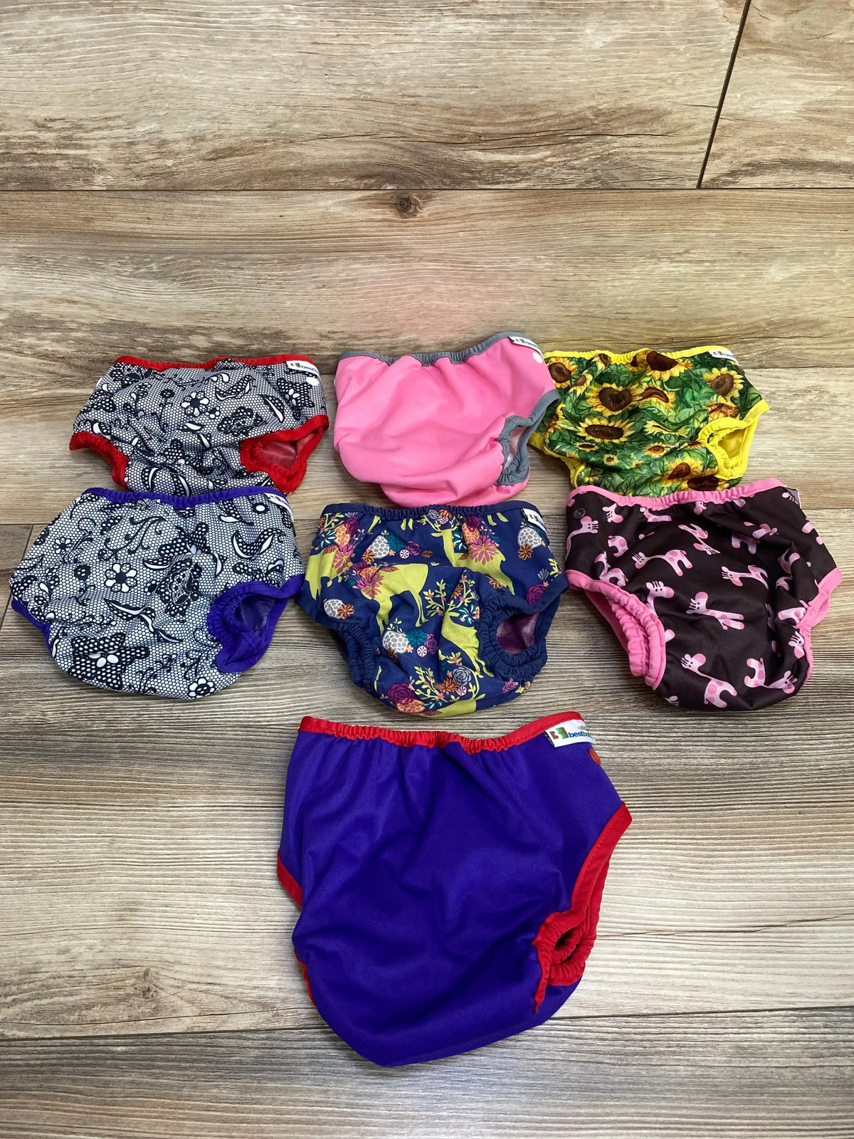 Top-down view of Best Bottom diaper covers 7-pack showing mixed prints and elastic leg openings on wood floor