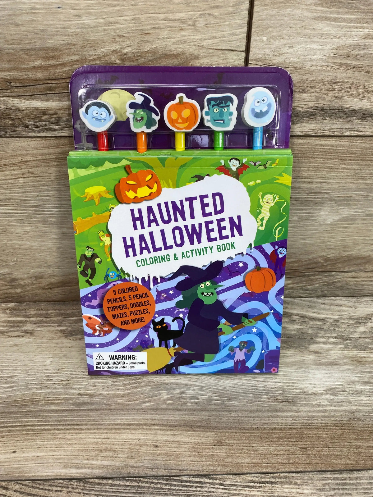 Front view of Haunted Halloween coloring book with 5 colored pencils and 5 Halloween pencil toppers on wood background