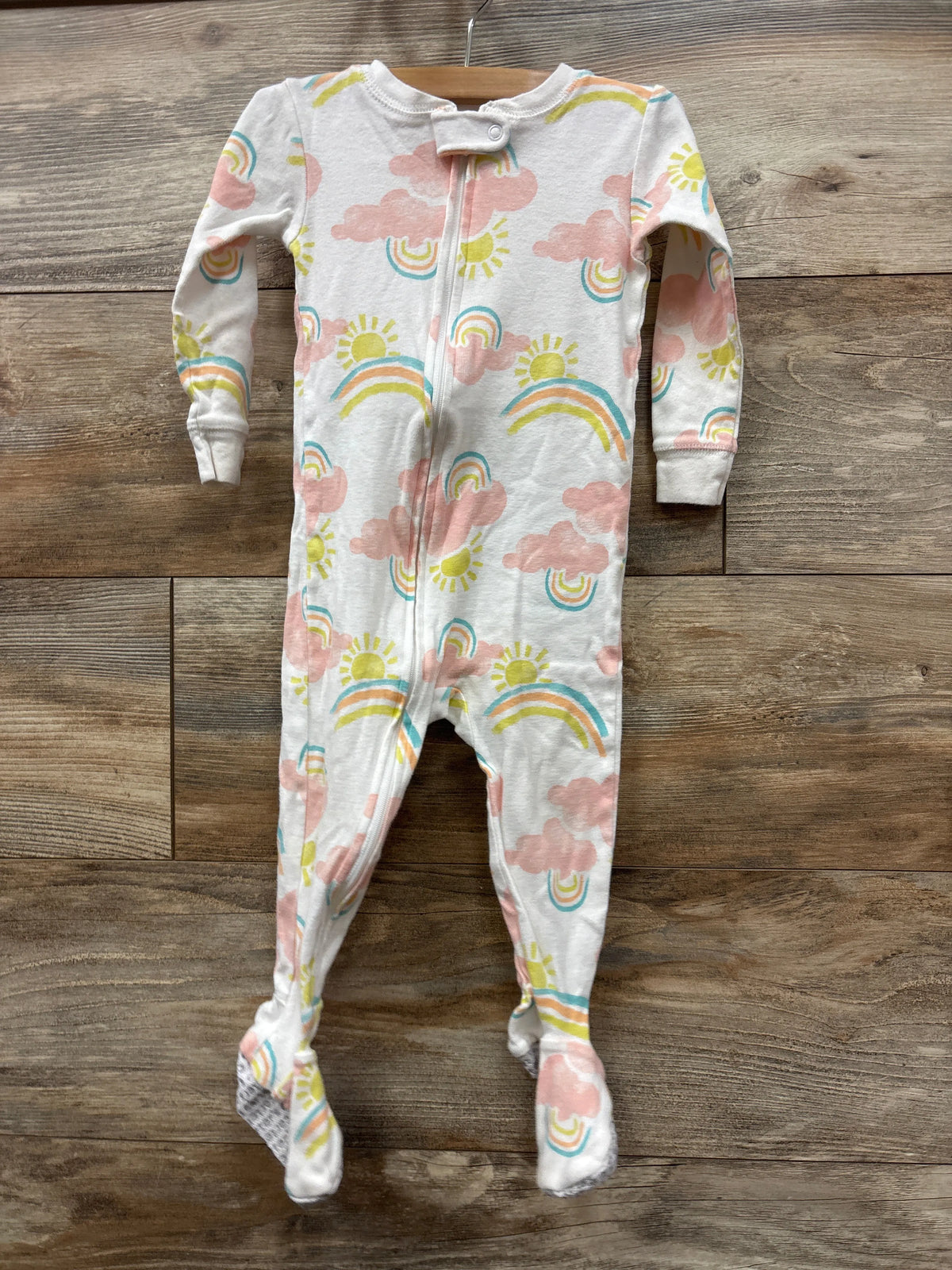 Front view of white Just One You sleeper, size 18 months, with rainbow and cloud print, zipper, and footed legs on wood