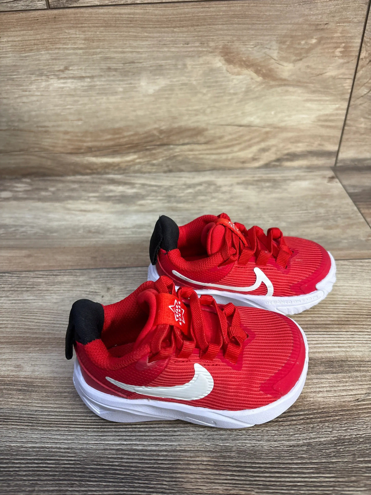 Top view of Nike Star Runner 4 TD sneakers showcasing red mesh uppers and white soles on a wood floor