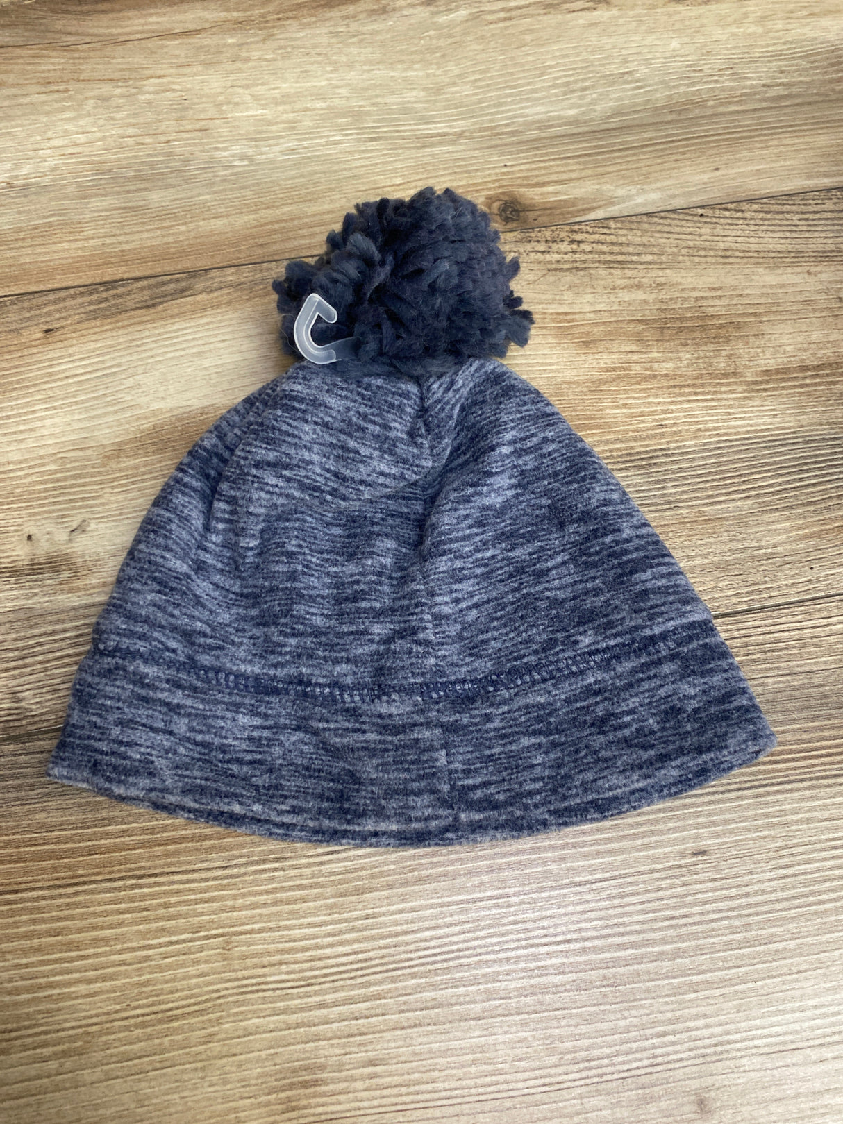 Blue and gray knit beanie hat with pom-pom on wooden surface