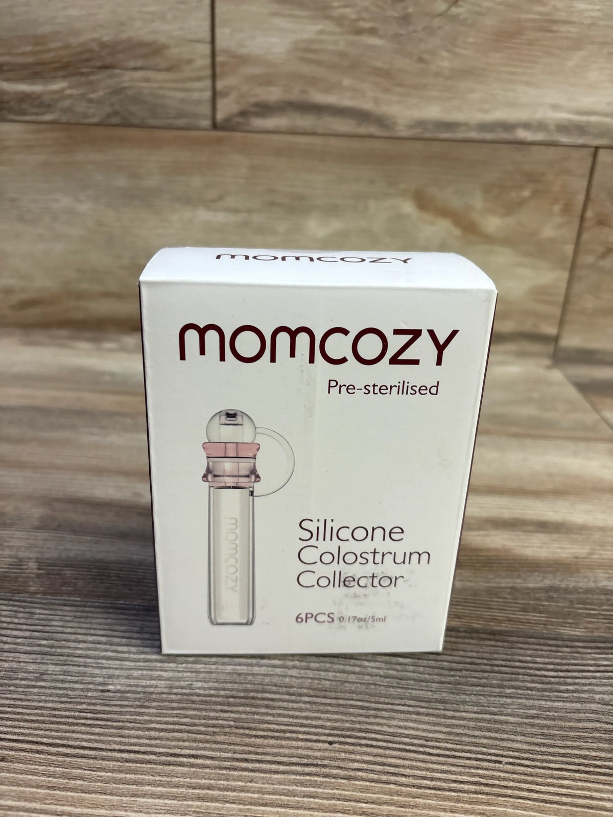 Front view of Momcozy silicone colostrum collector six-pack, pre-sterilised, 5 ml, on a wood-grain surface