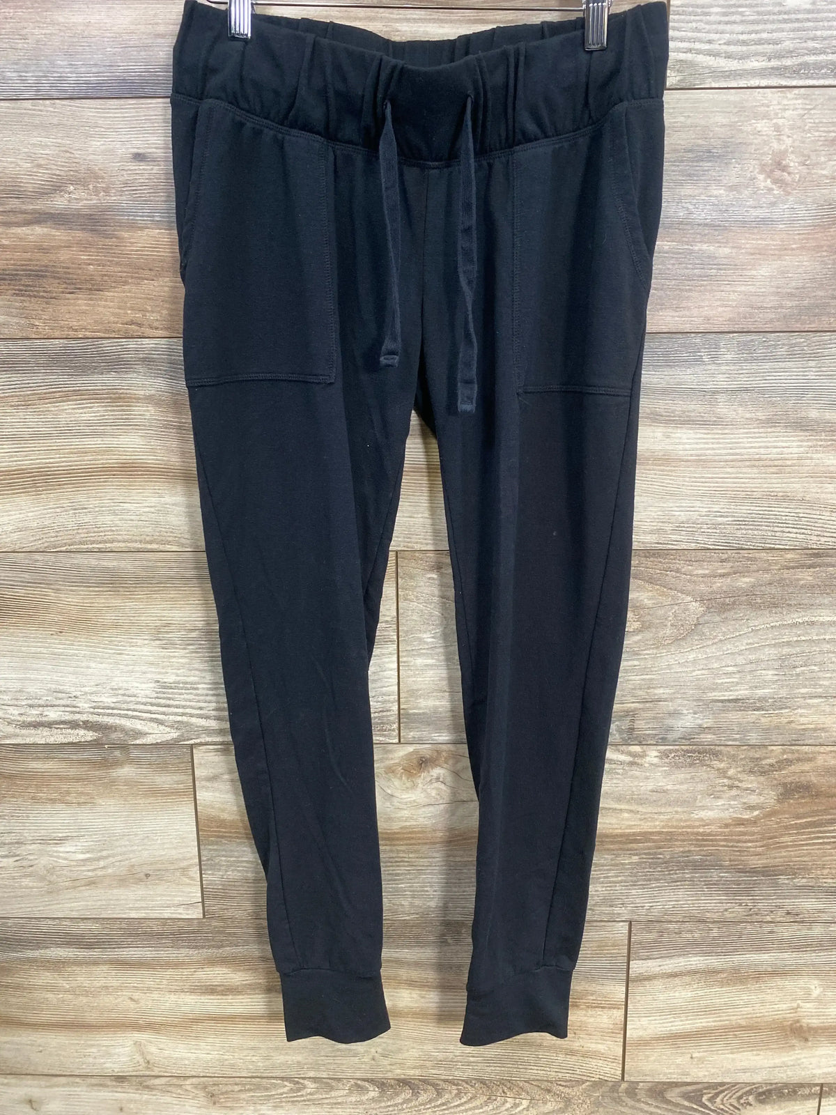 Front view of Isabel maternity joggers in black showing drawstring waistband, patch pockets and ribbed cuffs on wood background