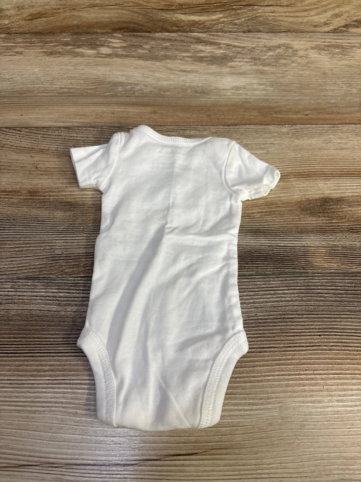 Front view of white Just One You dinosaur bodysuit showcasing short sleeves and leg openings on a wood background