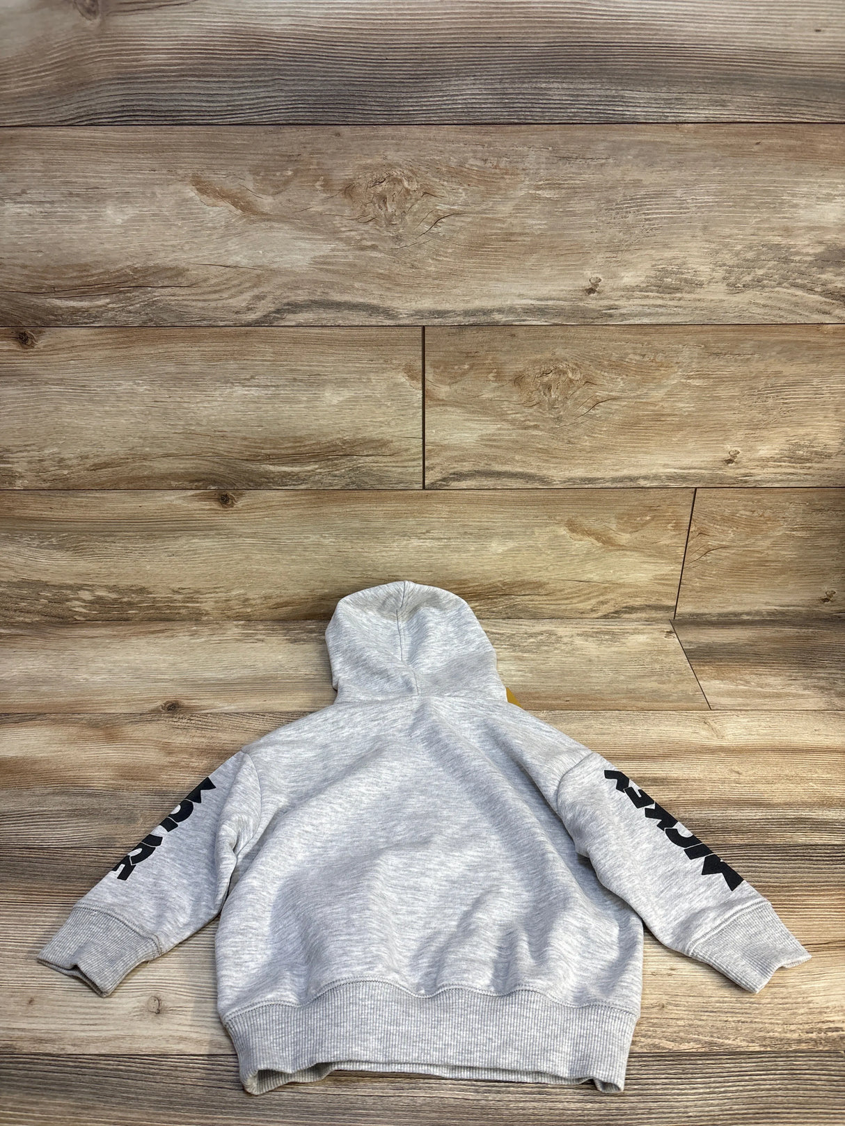 Gray kids hoodie with black sleeve graphics, laid flat on wood floor for resale