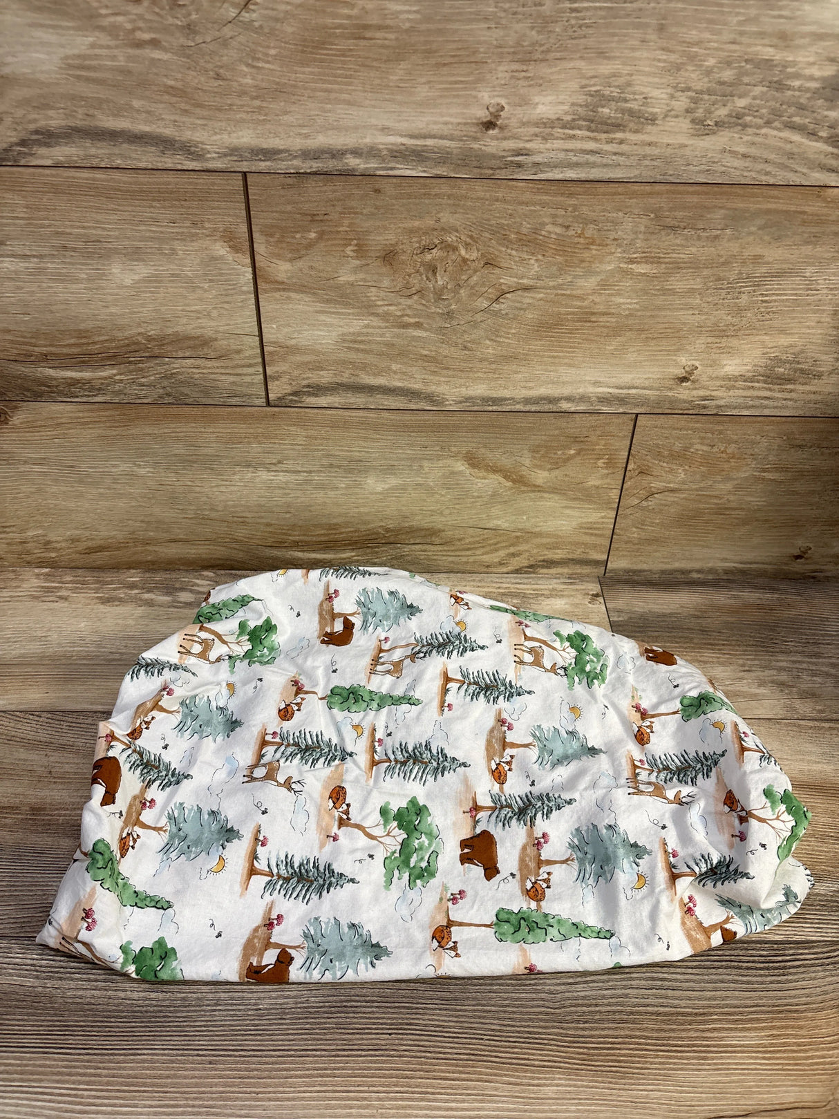 Top-down view of fitted bassinet sheet with woodland critters print (deer, fox, bear) on white background laid on wood surface