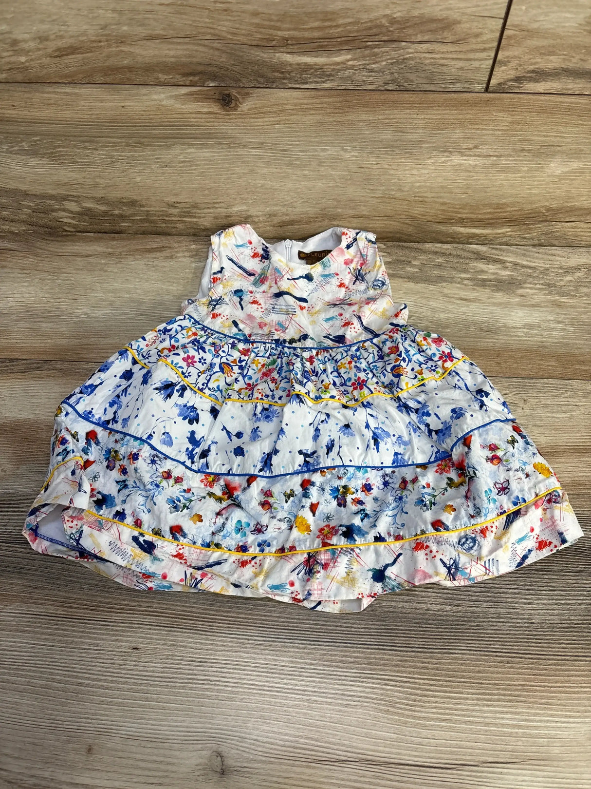 Flat lay of white toddler tiered dress with multicolor paint splatter and floral print, ruffled tiers on wood floor background