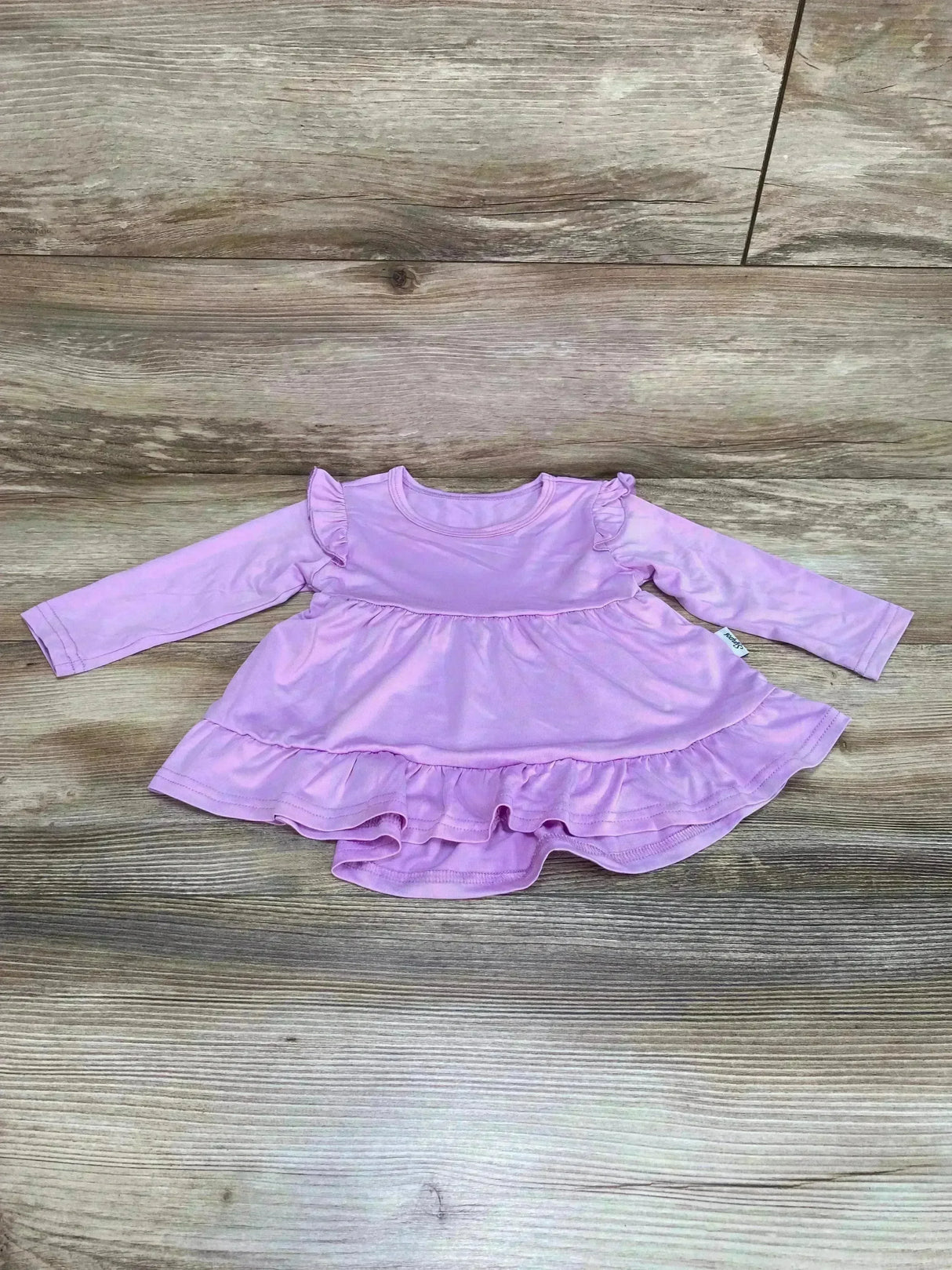 Flat lay of purple tiered ruffle baby dress showing long sleeves, ruffle shoulders and double ruffle hem on wood background
