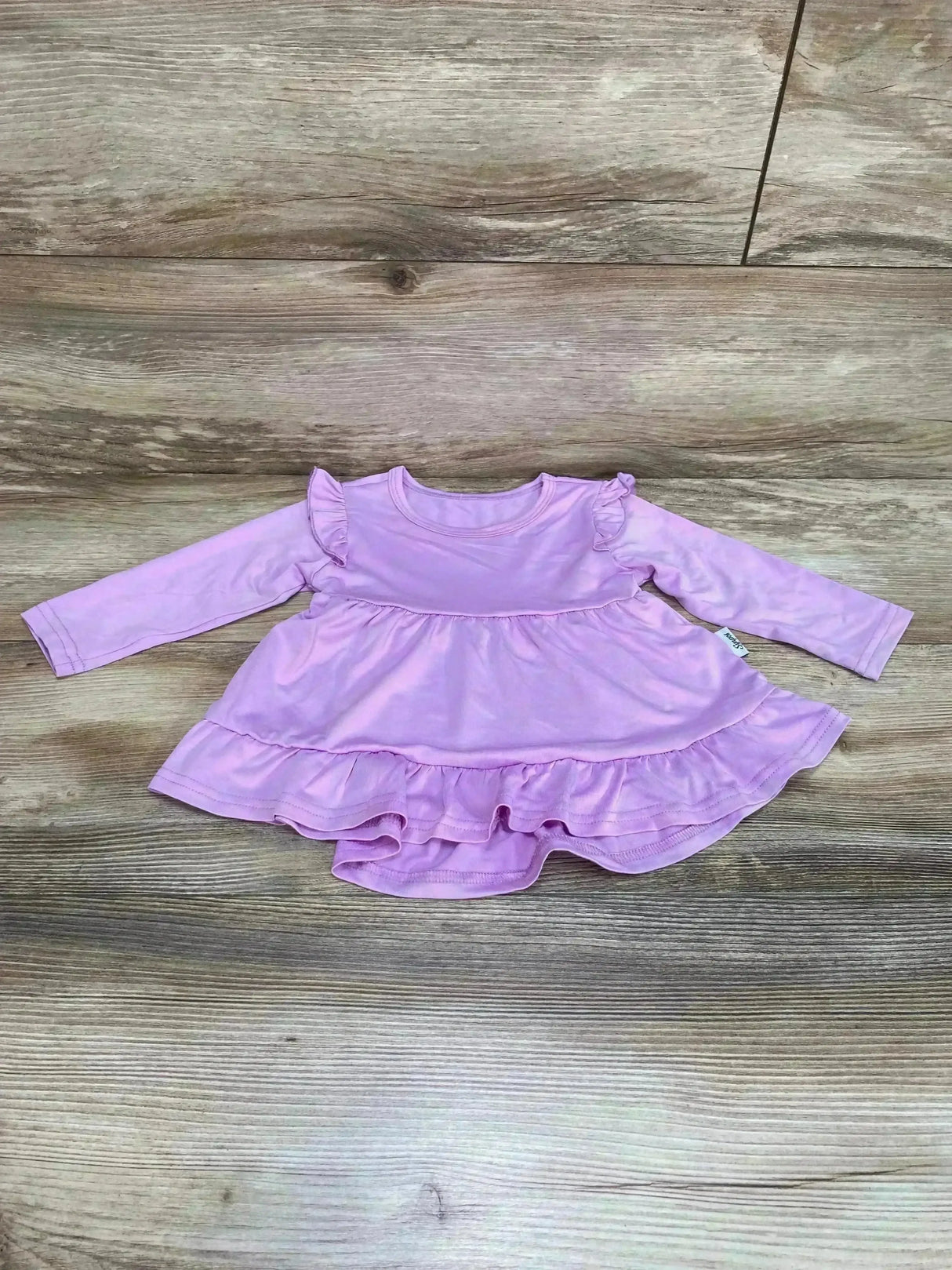 Flat lay of purple tiered ruffle baby dress showing long sleeves, ruffle shoulders and double ruffle hem on wood background