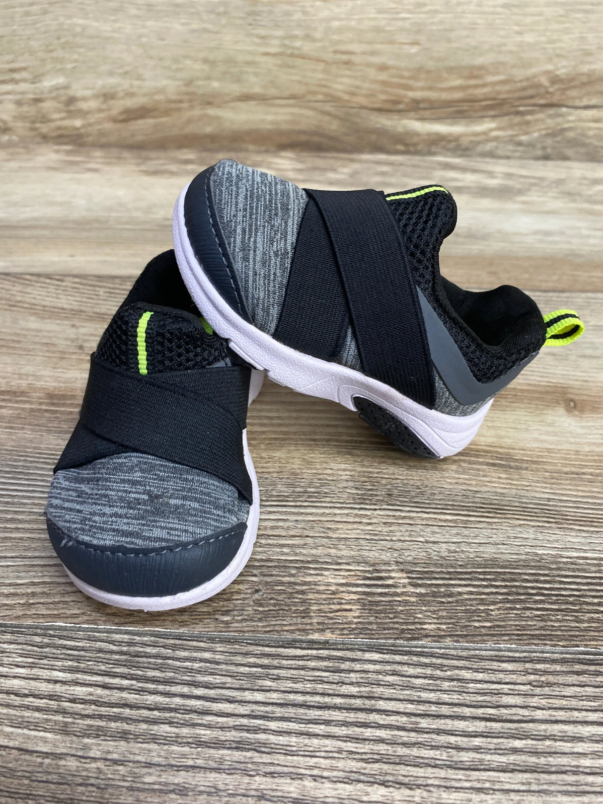 Kids slip-on sneakers, gray with black strap and neon trim, on wood background