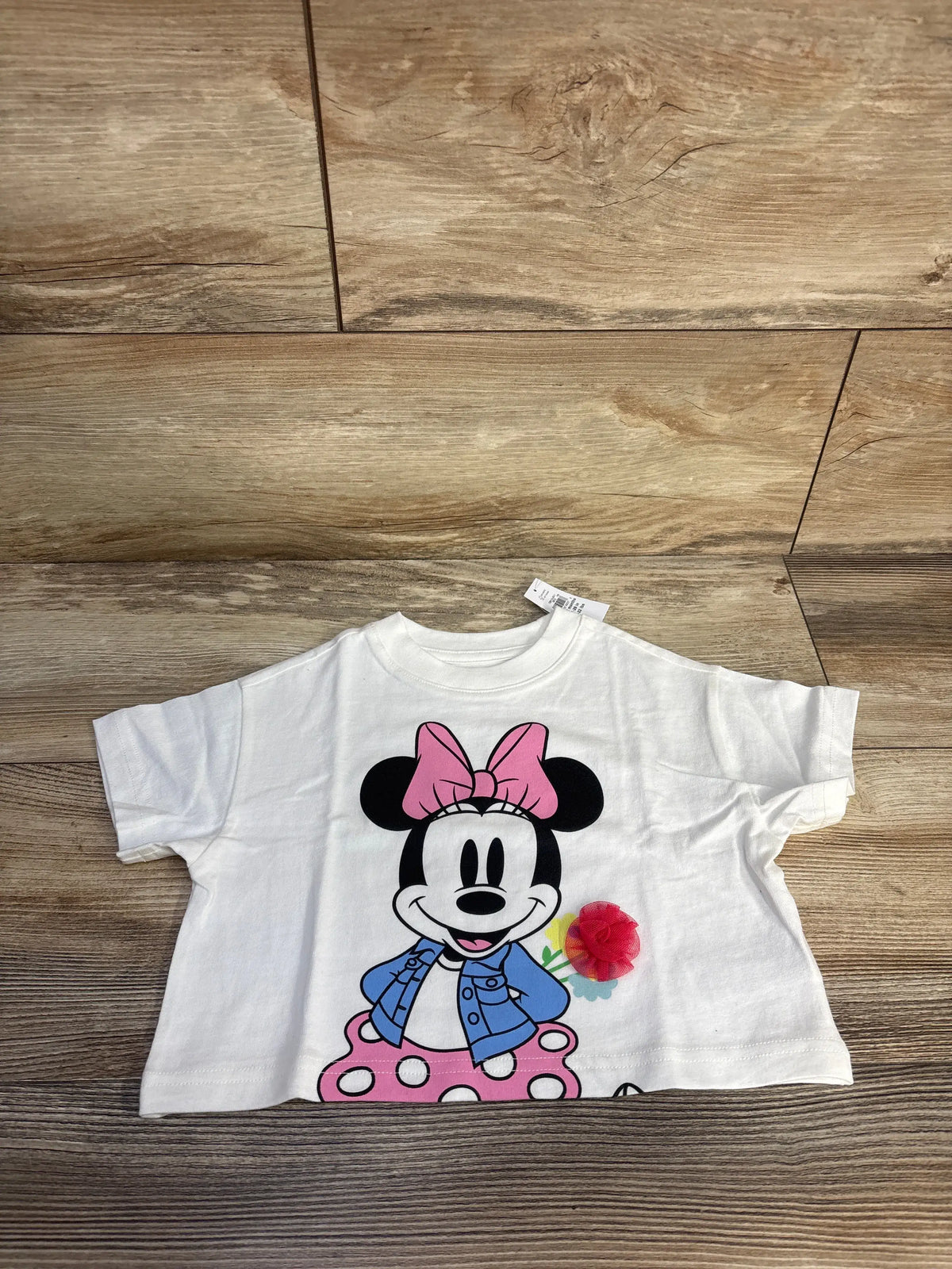 Front view of white Baby Gap Disney Minnie Mouse T-shirt showcasing a pink bow and blue jacket on a wood floor
