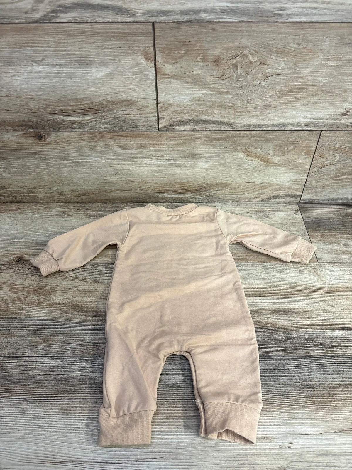 Soft beige baby onesie with long sleeves and footless legs, laid flat on wood floor