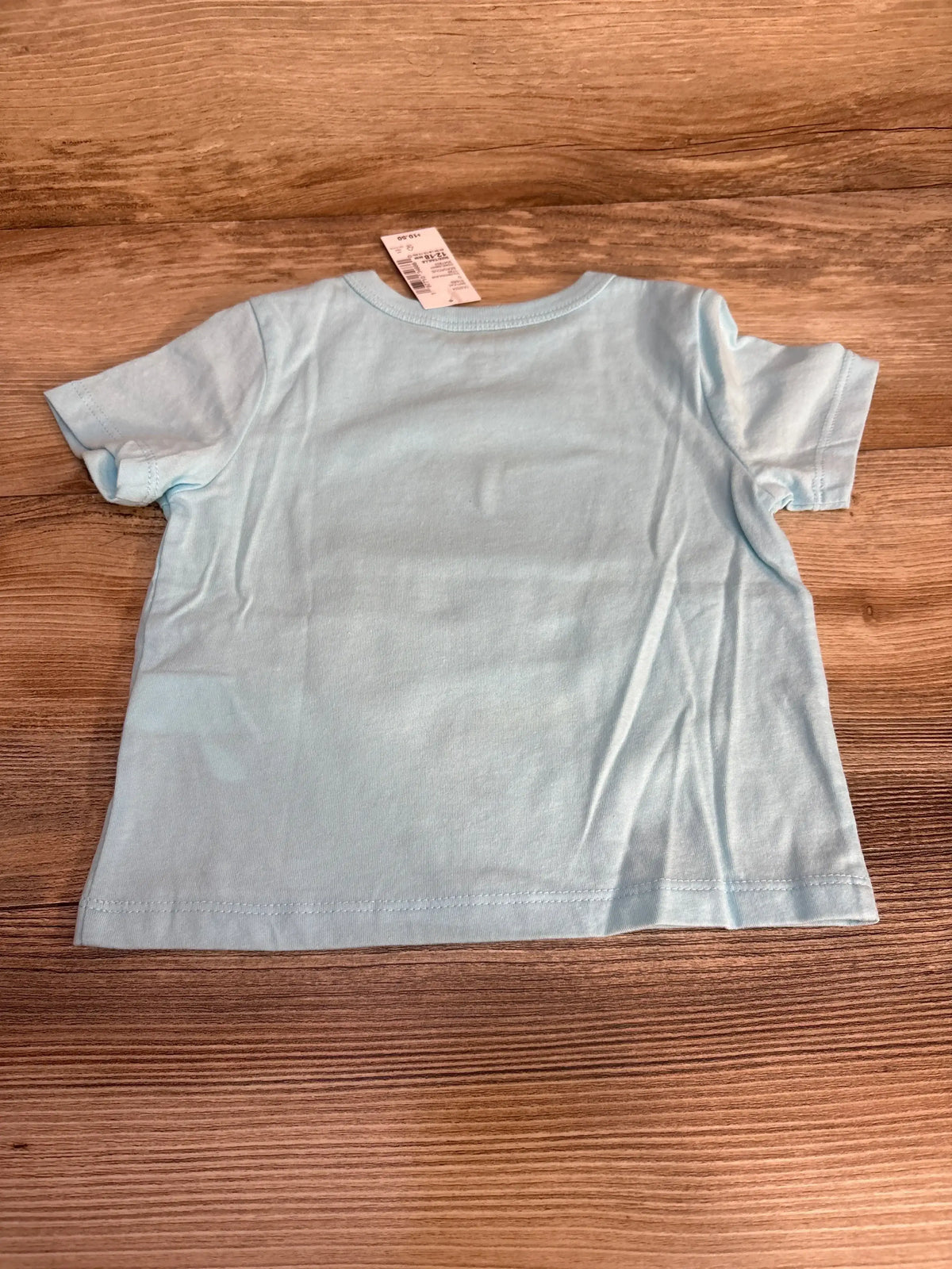 Back view of light blue toddler short-sleeve T-shirt showing size tag at neckline, flat on wood background
