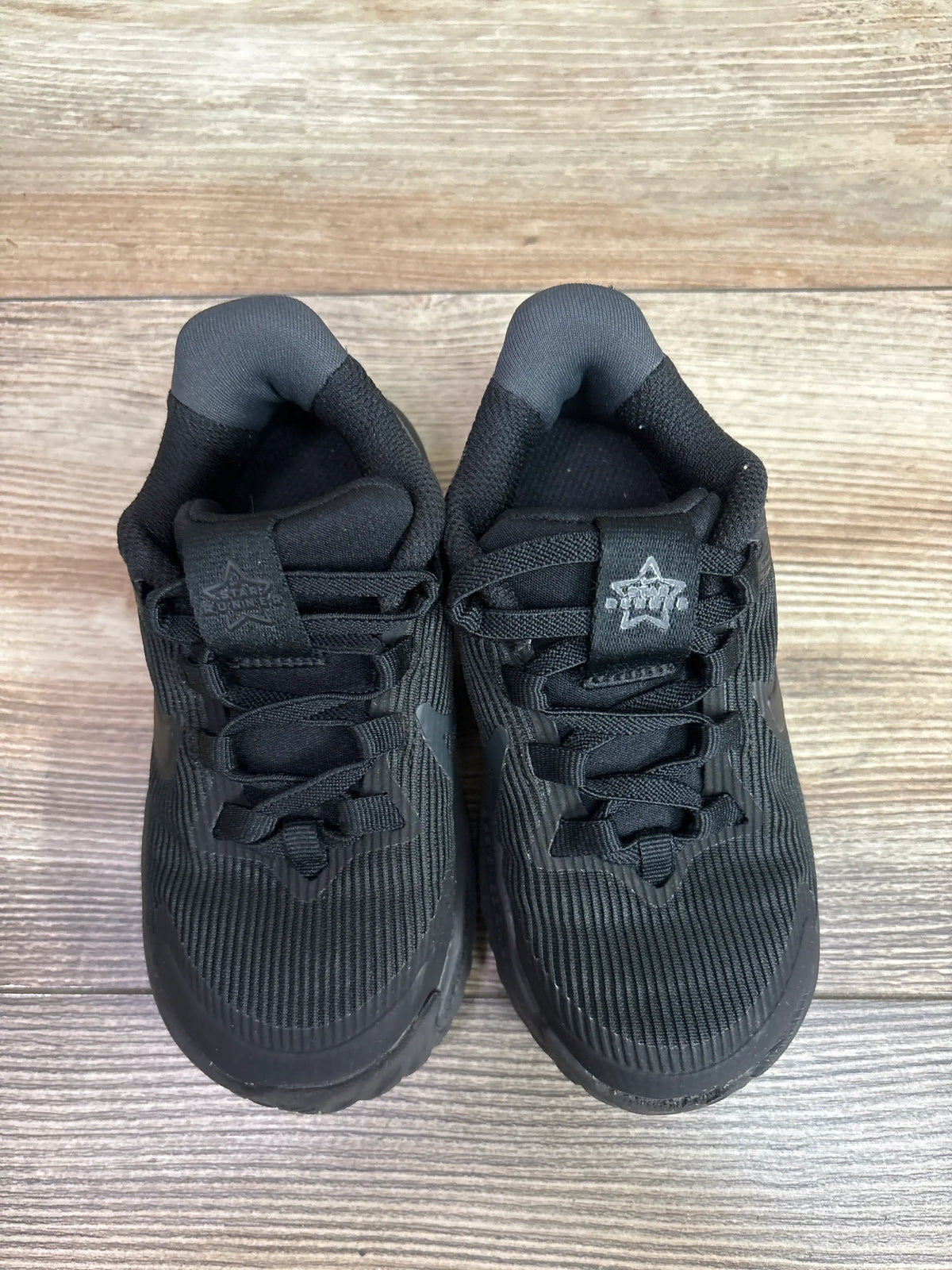 Top view of Nike Star Runner 4 TD Triple Black sneakers size 8c on a wooden surface.