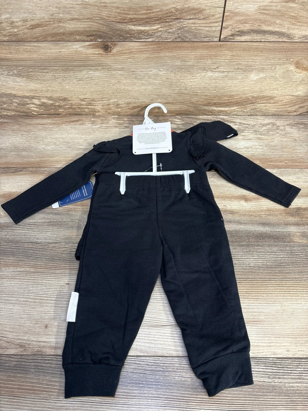 Front view of black 3-piece Boo Crew baby set, size 12 months, with long-sleeve top and pants on wood flooring