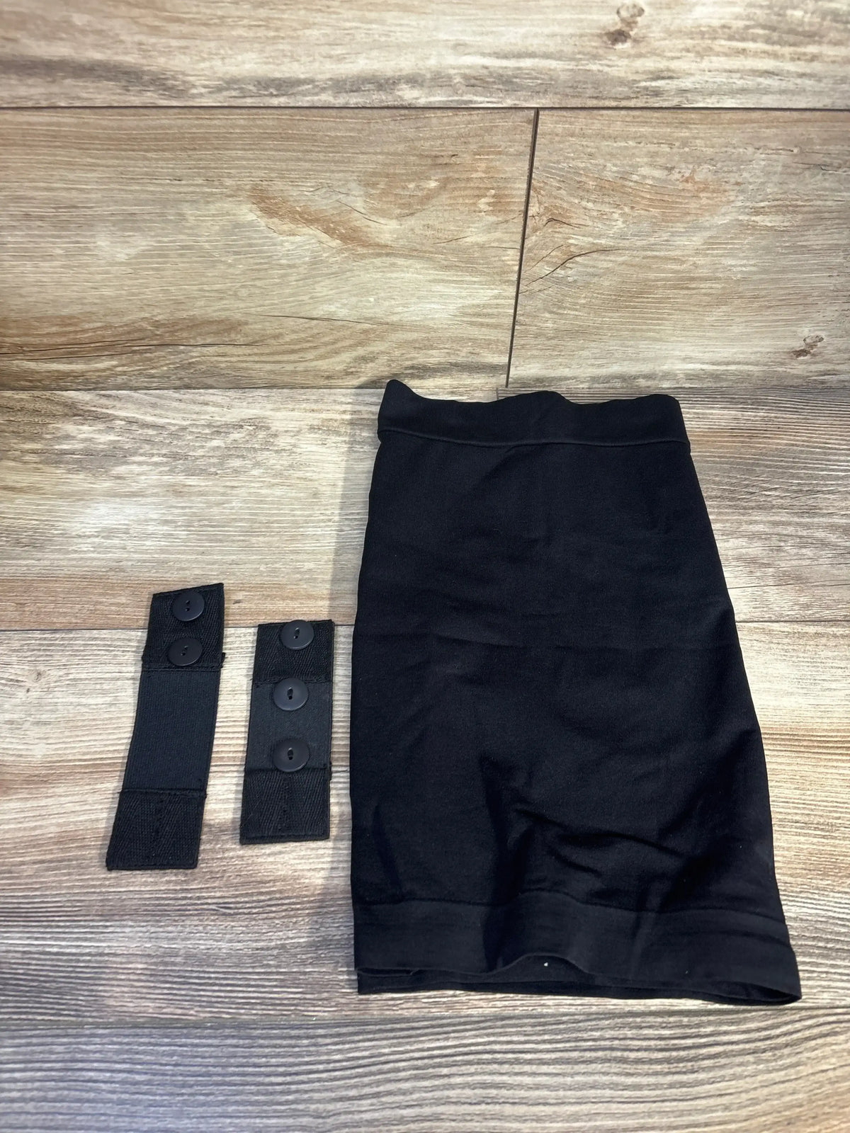 Flat lay of Kunindome black maternity belly band with two waist extenders showing elastic panel and button closures on wood