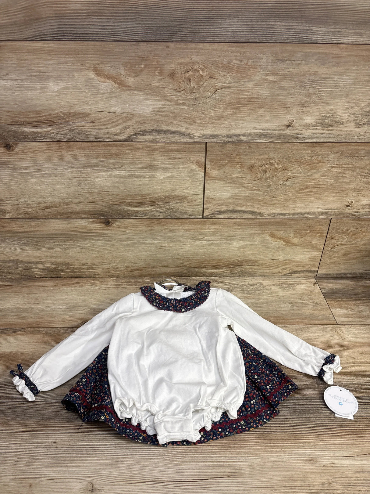 Long sleeve white baby romper with floral ruffle trim and matching skirt on wood background