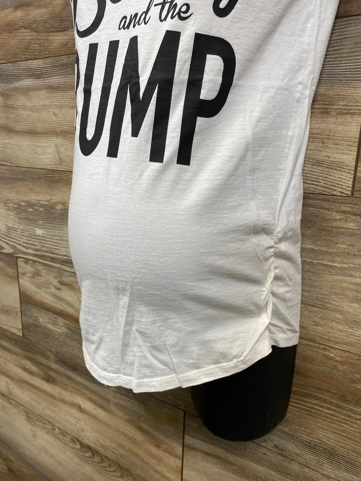 White maternity t-shirt with black text standing against wooden panel background