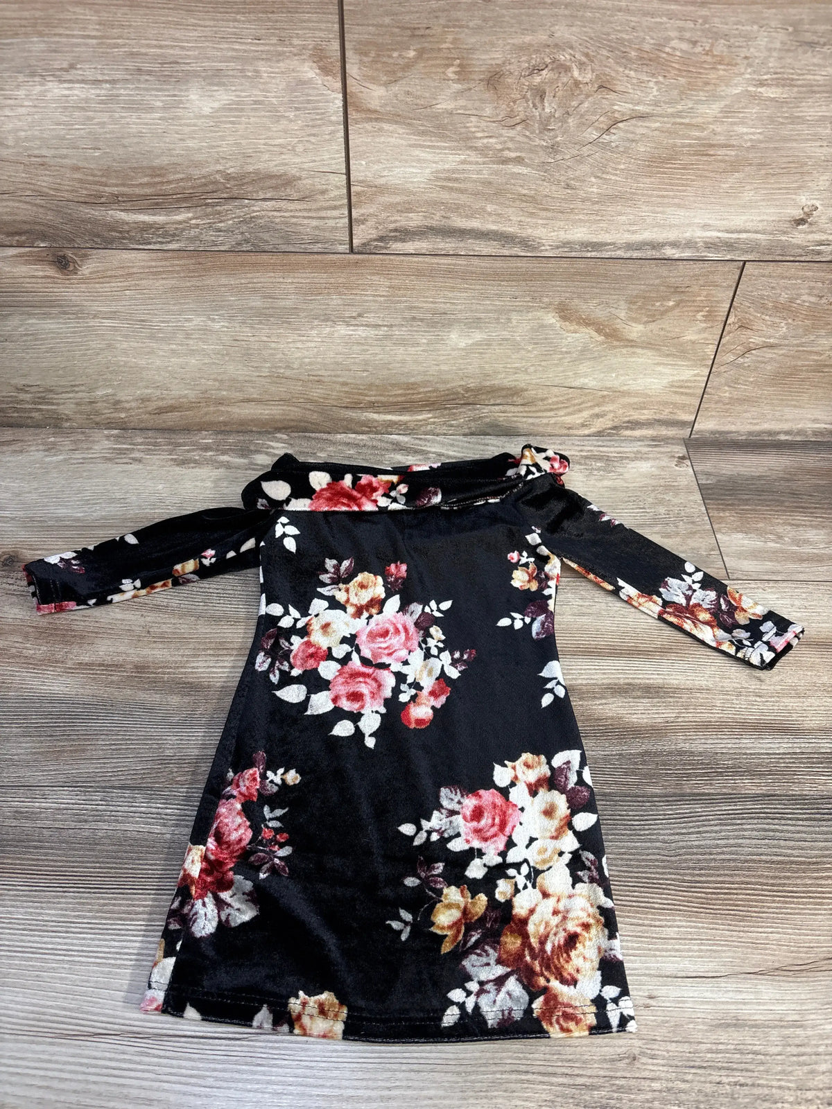 Front view of black toddler dress showcasing floral velvet print, off-shoulder neckline, and long sleeves on wood floor