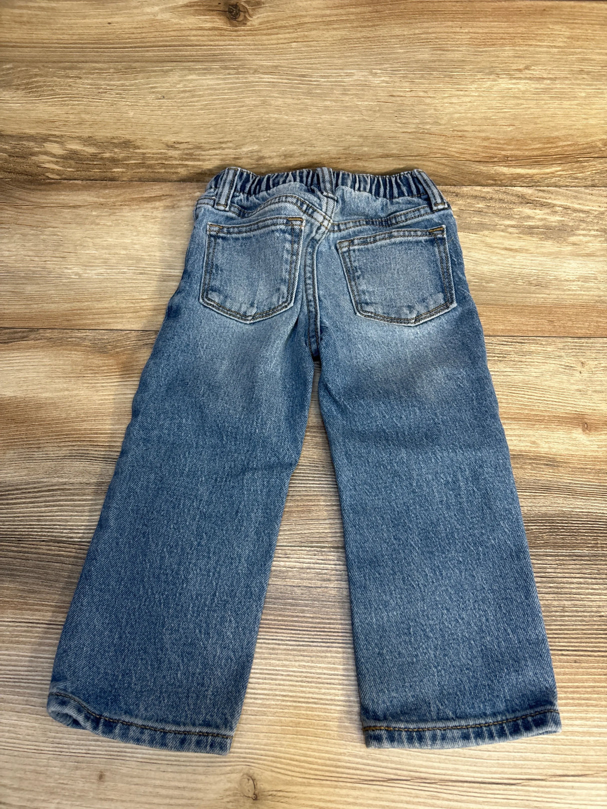 Back view of kids' blue denim jeans with elastic waistband on wooden background