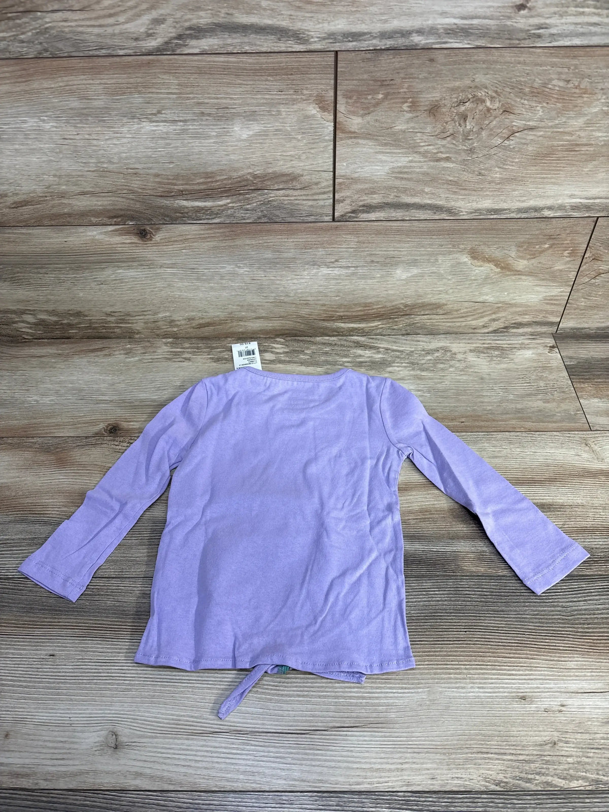Back view of a light purple long-sleeve toddler shirt on wood background