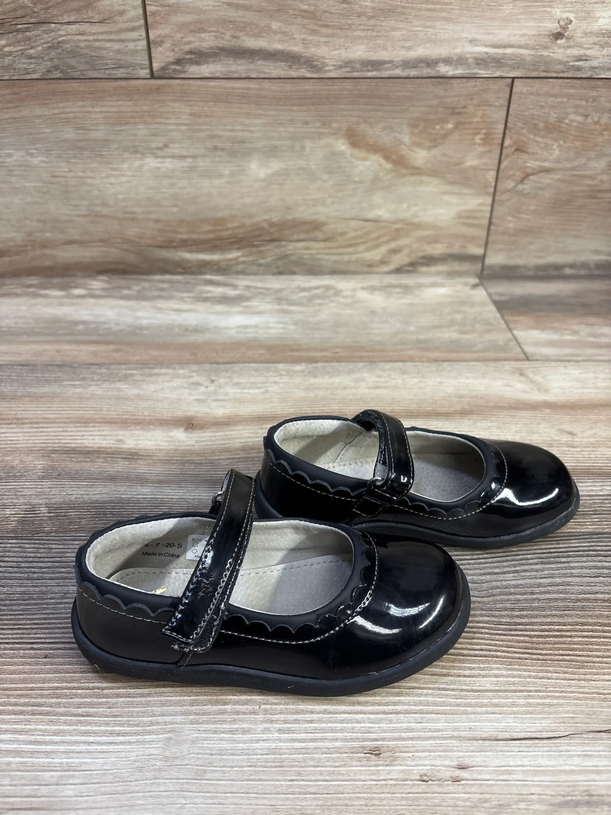 Side view of See Kai Run Jane Mary Jane toddler shoes, black patent leather, scalloped trim and Velcro strap on wood floor