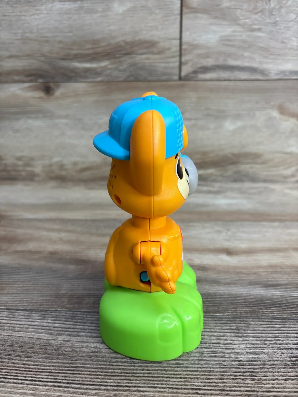 Side view of Fisher-Price Link Squad Opposites Fox toy showcasing orange figure with blue baseball cap on green grass base on wood floor