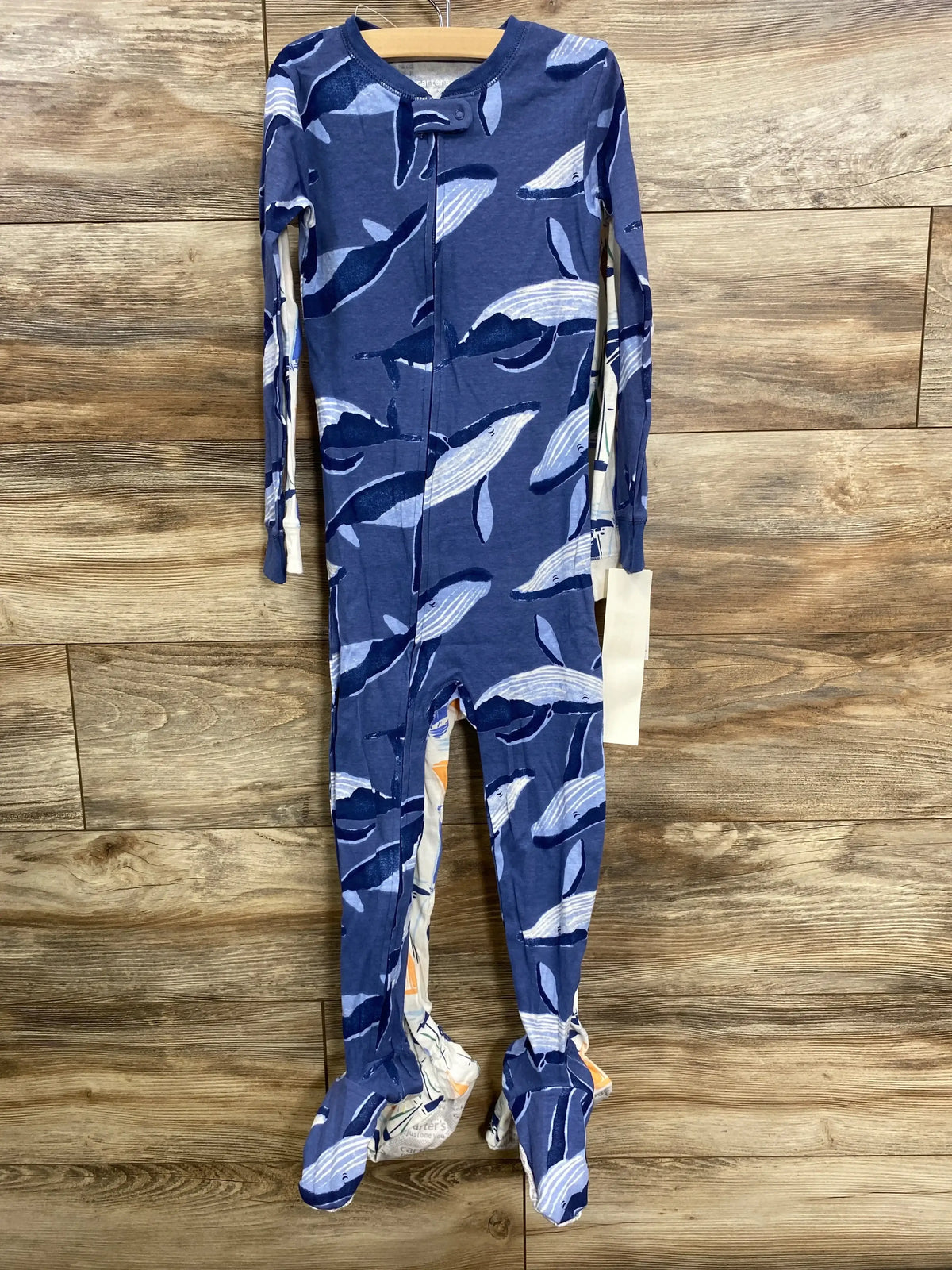 Blue baby footed pajama with whale pattern hanging on wooden wall
