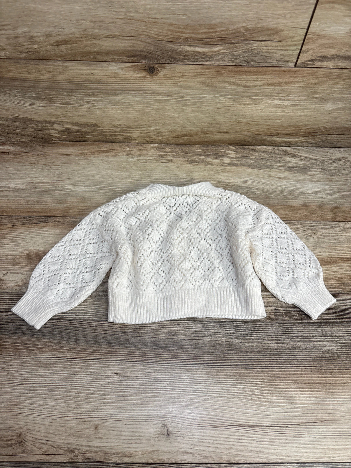 White knitted baby sweater with diamond pattern and ribbed cuffs and hem on wooden surface
