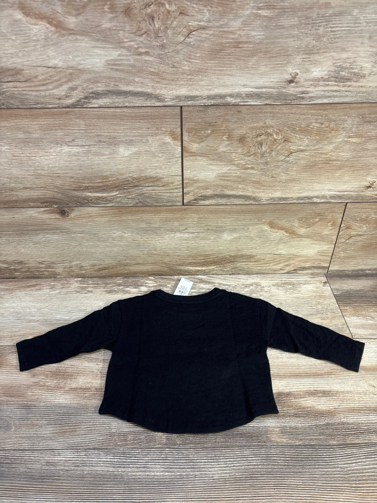 Back view of Baby Gap black graphic swan shirt, size 6 to 12 months, with long raglan sleeves on wood look flooring