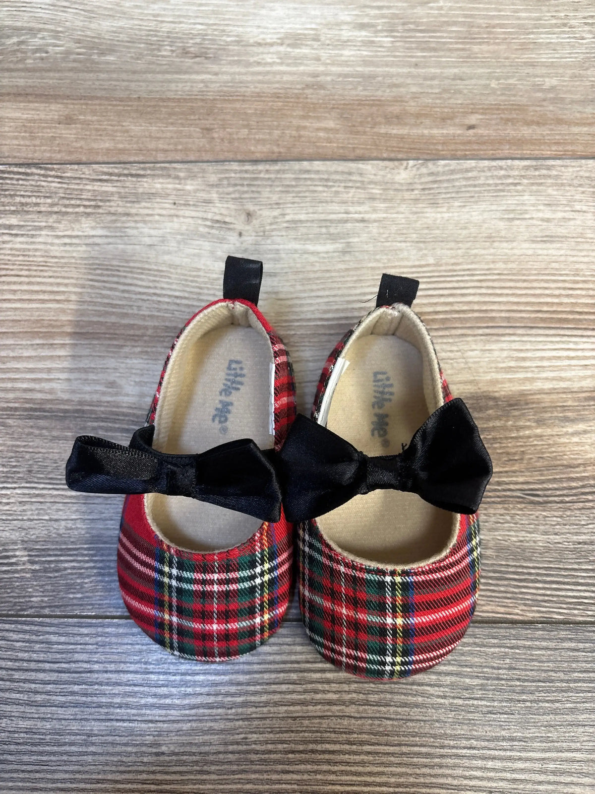 Top view of Little Me Soft Sole Tartan Mary Jane flats showing red tartan plaid and black bow straps on a wooden floor