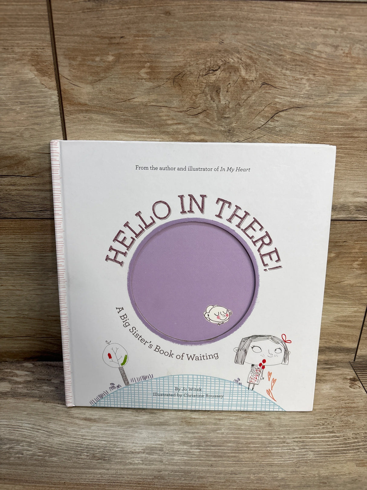 Front cover of Hello in There! hardcover children's book with purple circular peek-through and illustrated girl on wood background