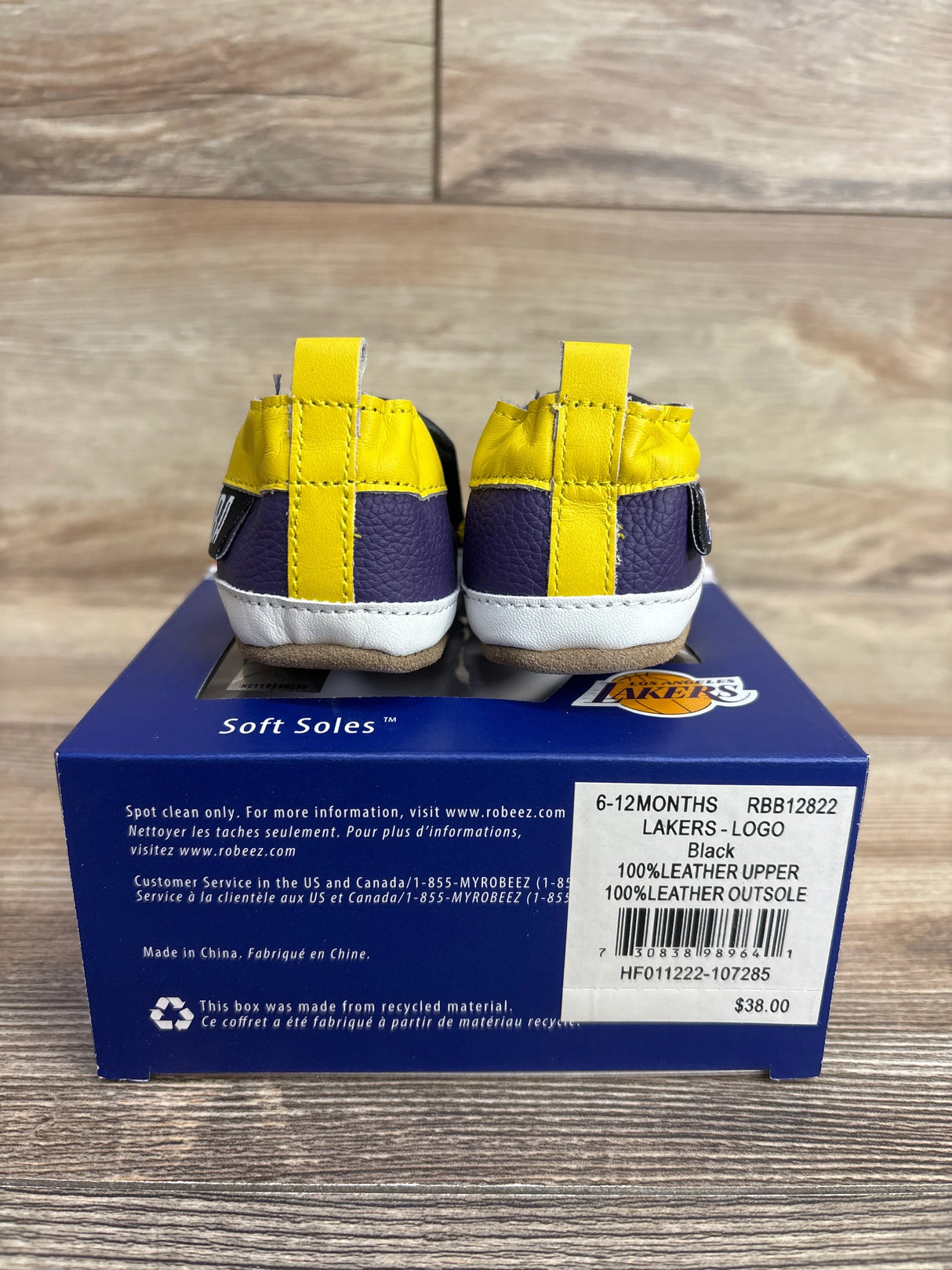 Baby shoes in purple, yellow, and white leather displayed on a blue box with Los Angeles Lakers logo, size 6-12 months