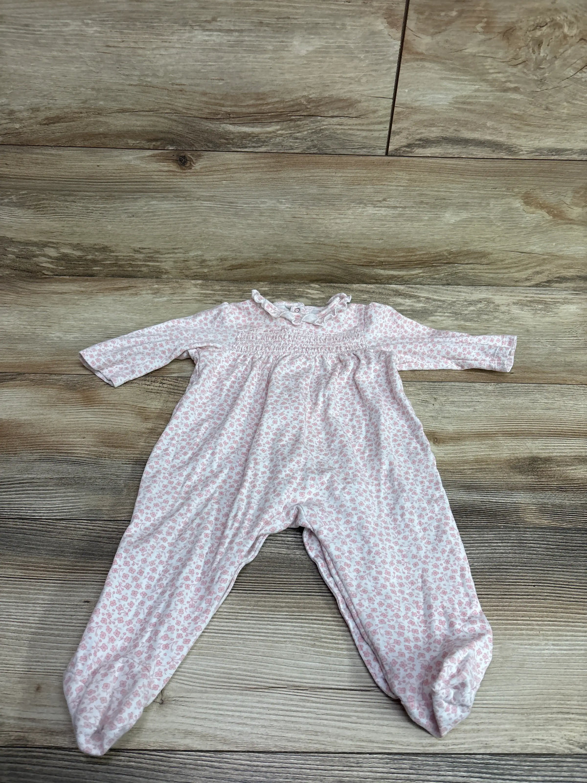 Front view of Little Me smocked footed coverall with long sleeves, floral pattern, smocked bodice, and footed legs on wood-look floor