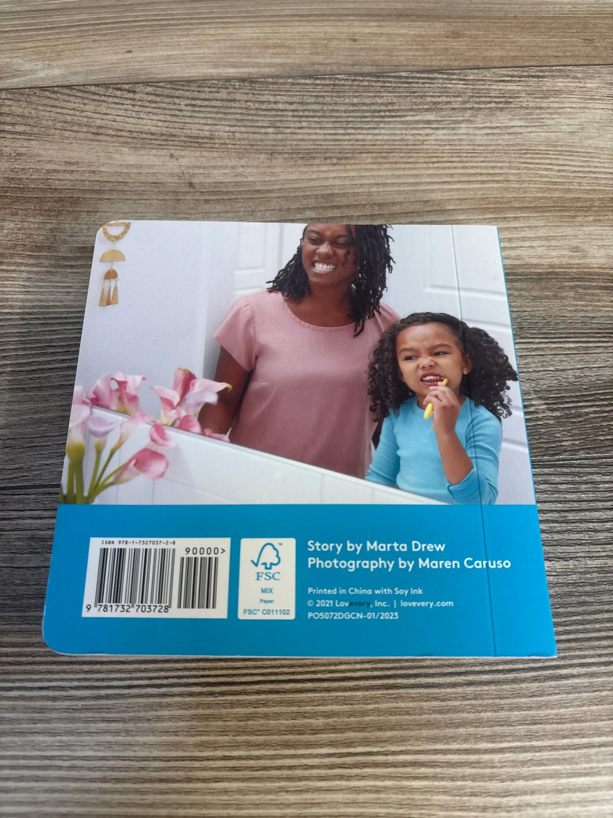 Back of Lovevery Now That I’m Three board book showing parent and child brushing teeth, barcode and credits on wood table