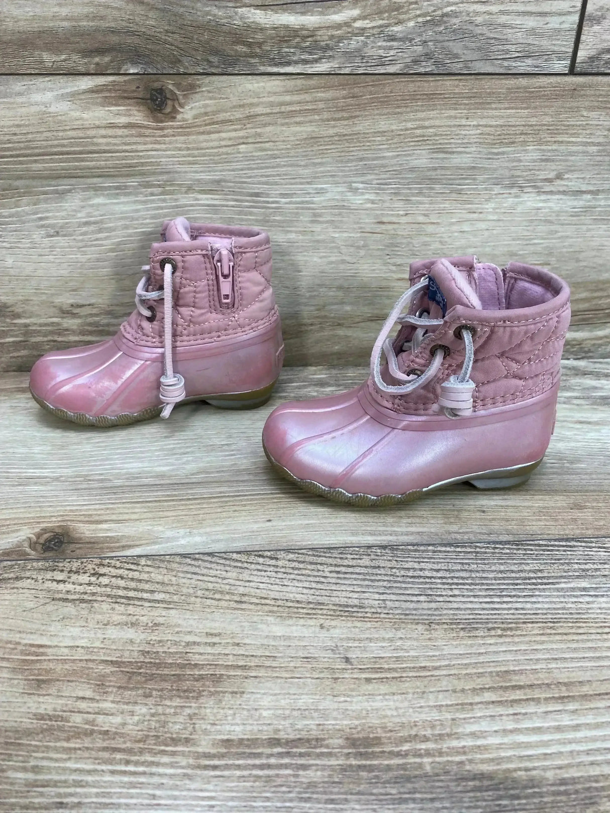 Side view of toddler pink Sperry Saltwater duck boots showing quilted shaft, side zipper, drawstring closure on wood floor
