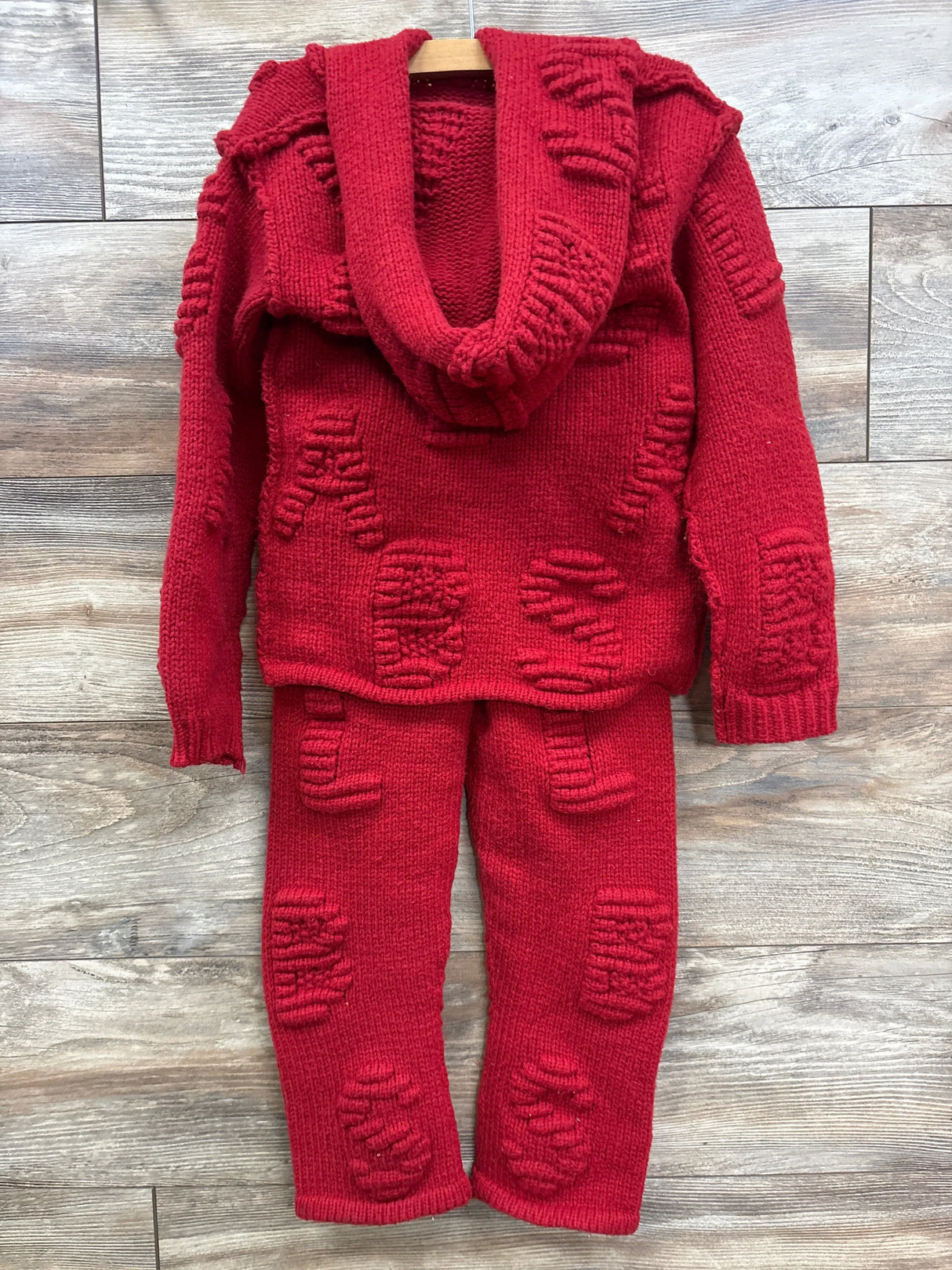 Red knit children's sweater and pants set with textured letter patterns, on wood floor