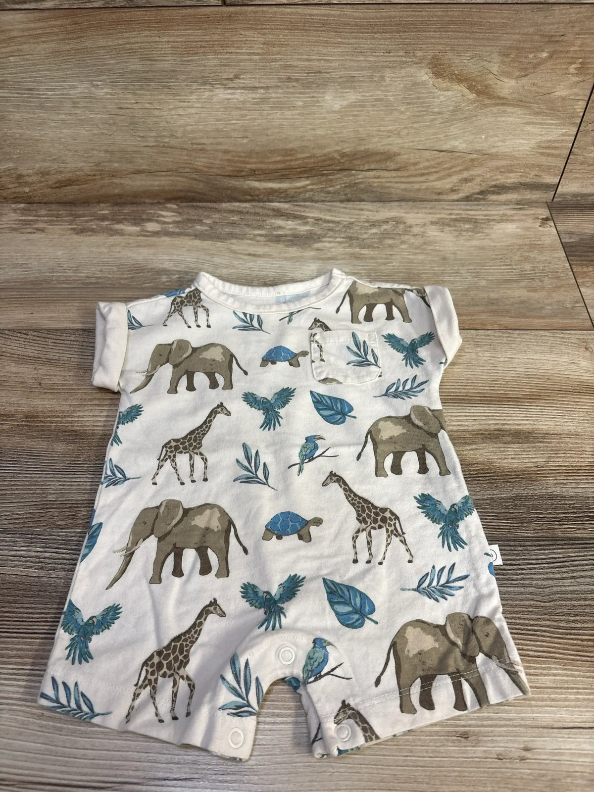 Flat lay of beige Little Planet organic romper with animal print and crotch snaps on wood background