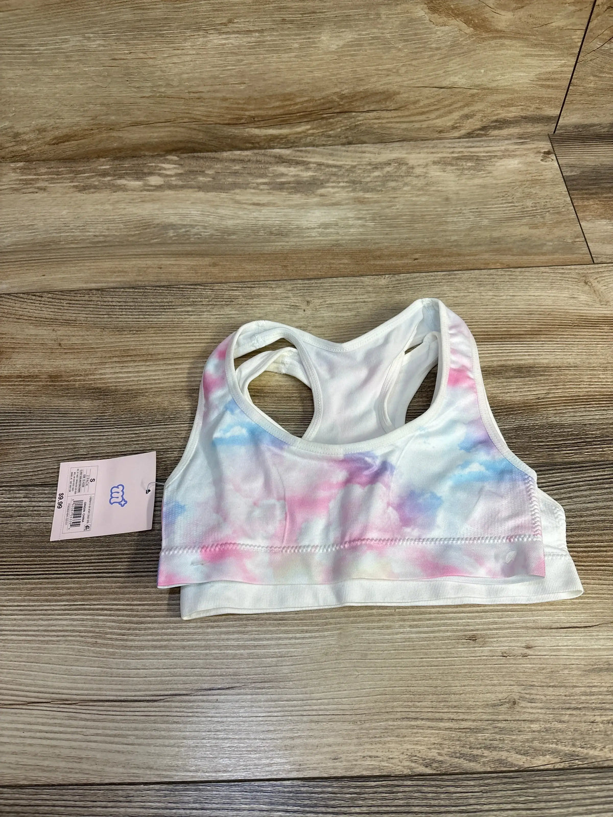 Tie dye sports bra with pink and blue pattern and tag on wood floor background