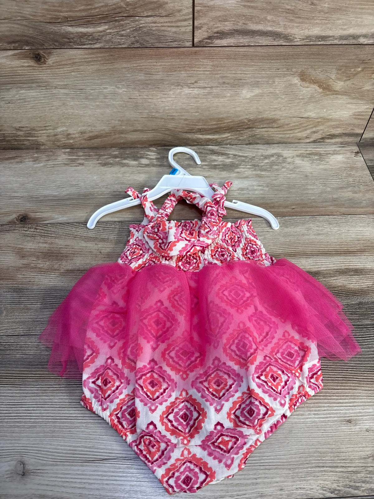 Flat lay of pink smocked bodysuit dress with tulle skirt and matching headband on white hanger on wood background, size 24 months