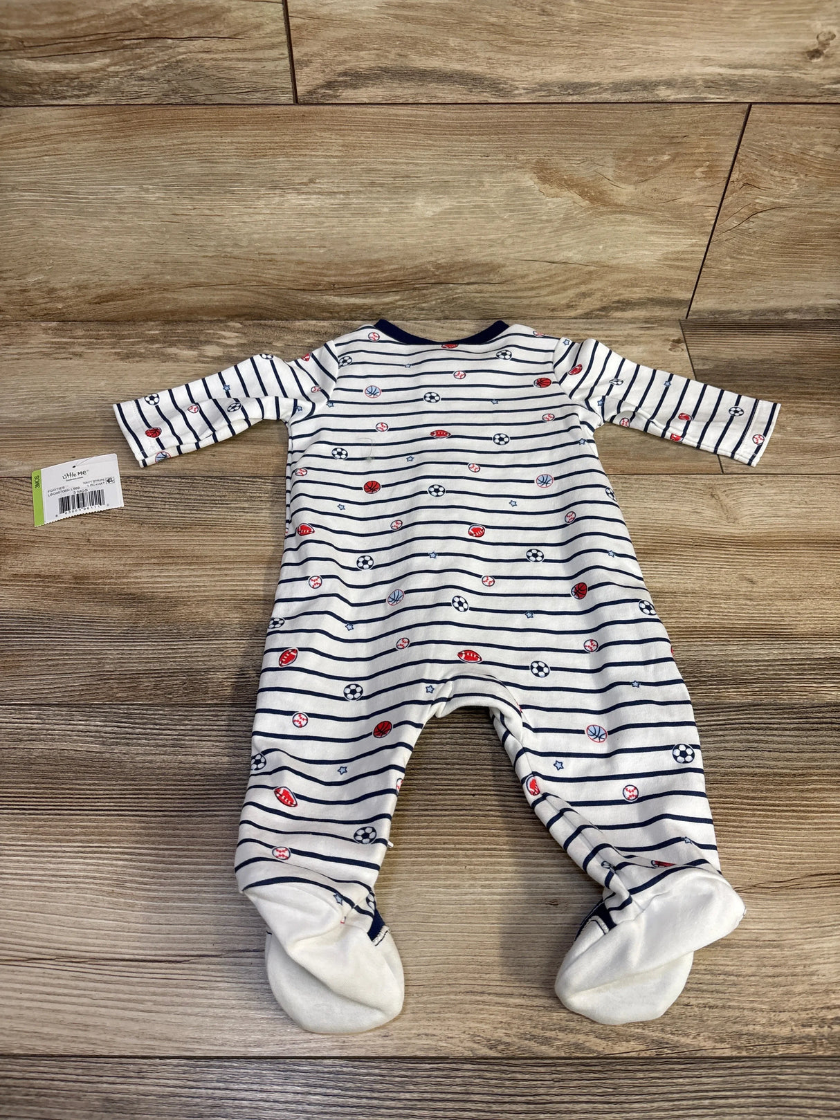 Flat lay of Little Me white footed sleeper showcasing navy stripes and red and navy sports ball prints on wood floor