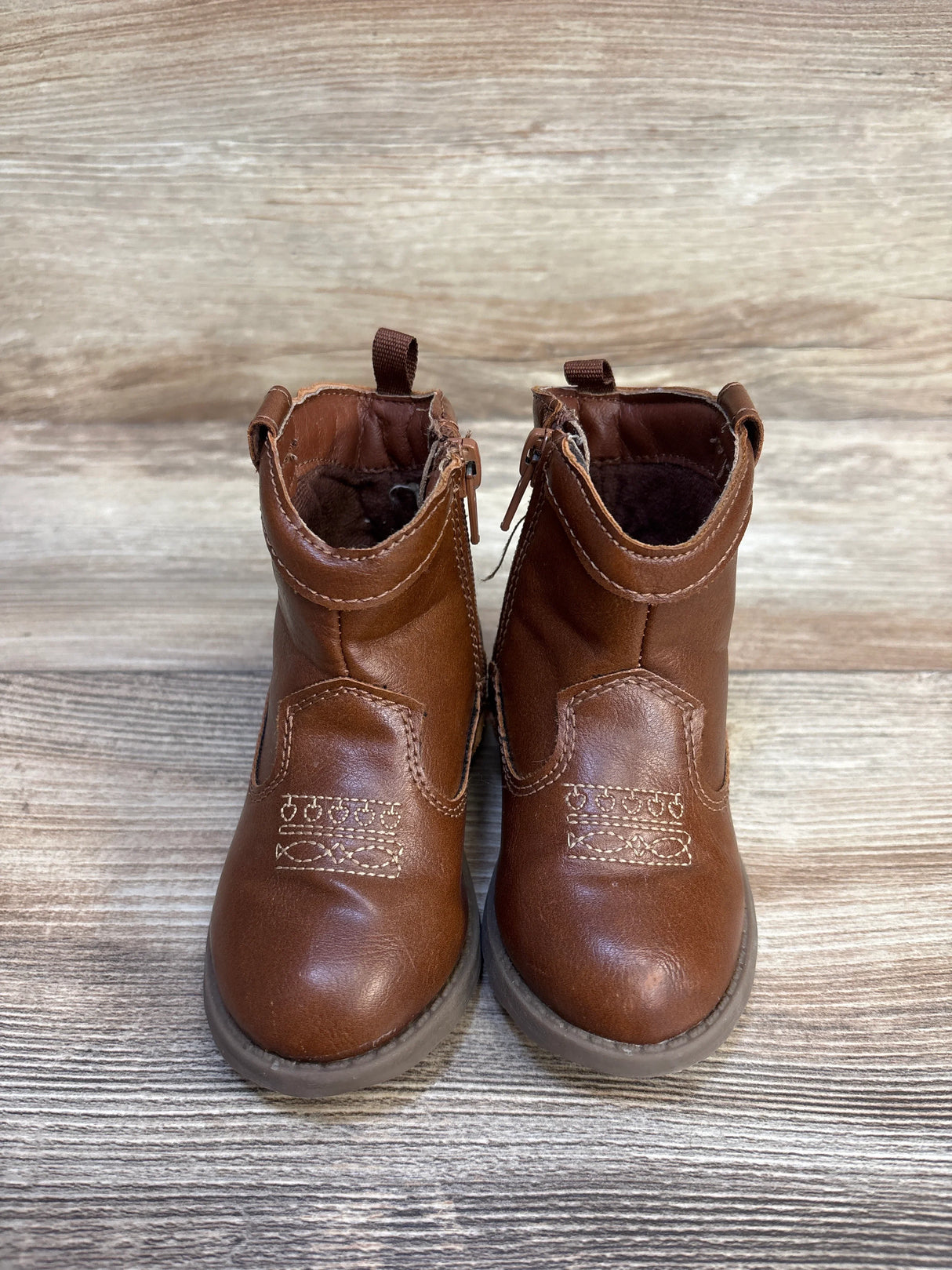 Brown toddler cowboy boots with decorative stitching on wood background