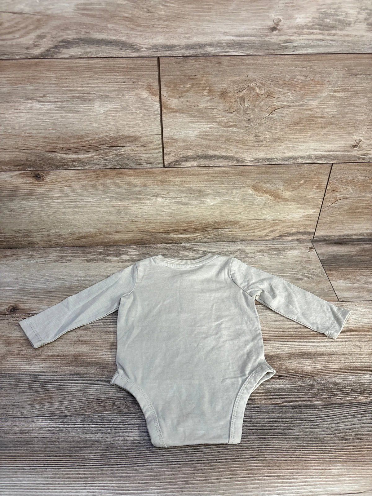 Front view of Telluride cream Henley bodysuit showcasing long sleeves and a Henley neckline on a wood-look floor