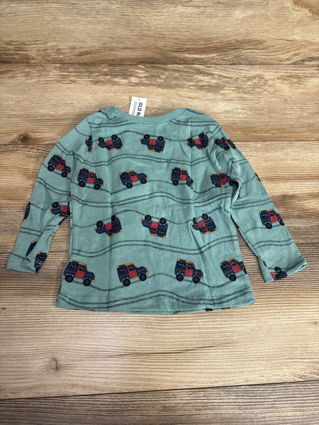 Green long sleeve toddler shirt with colorful truck print, laid flat on wood background