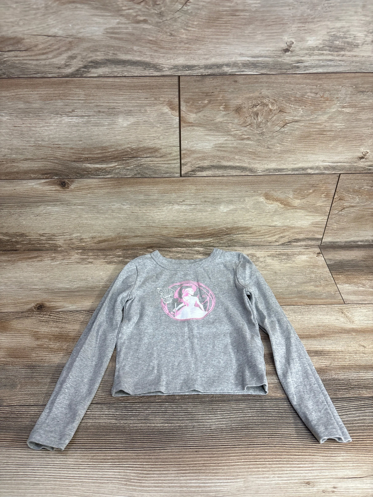 Gray long sleeve girls shirt with pink fairy graphic, laid flat on wooden floor