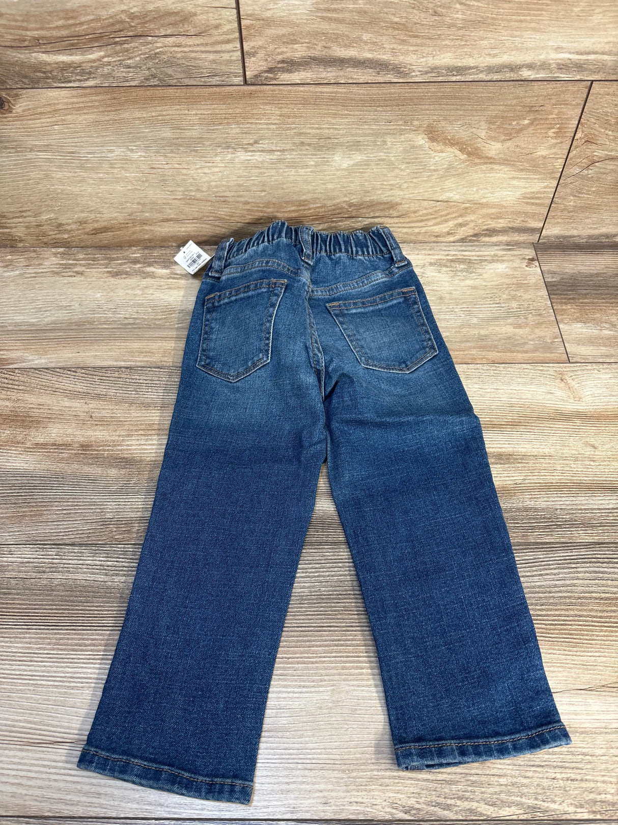Rear view of kids' blue denim jeans with elastic waistband on wooden floor