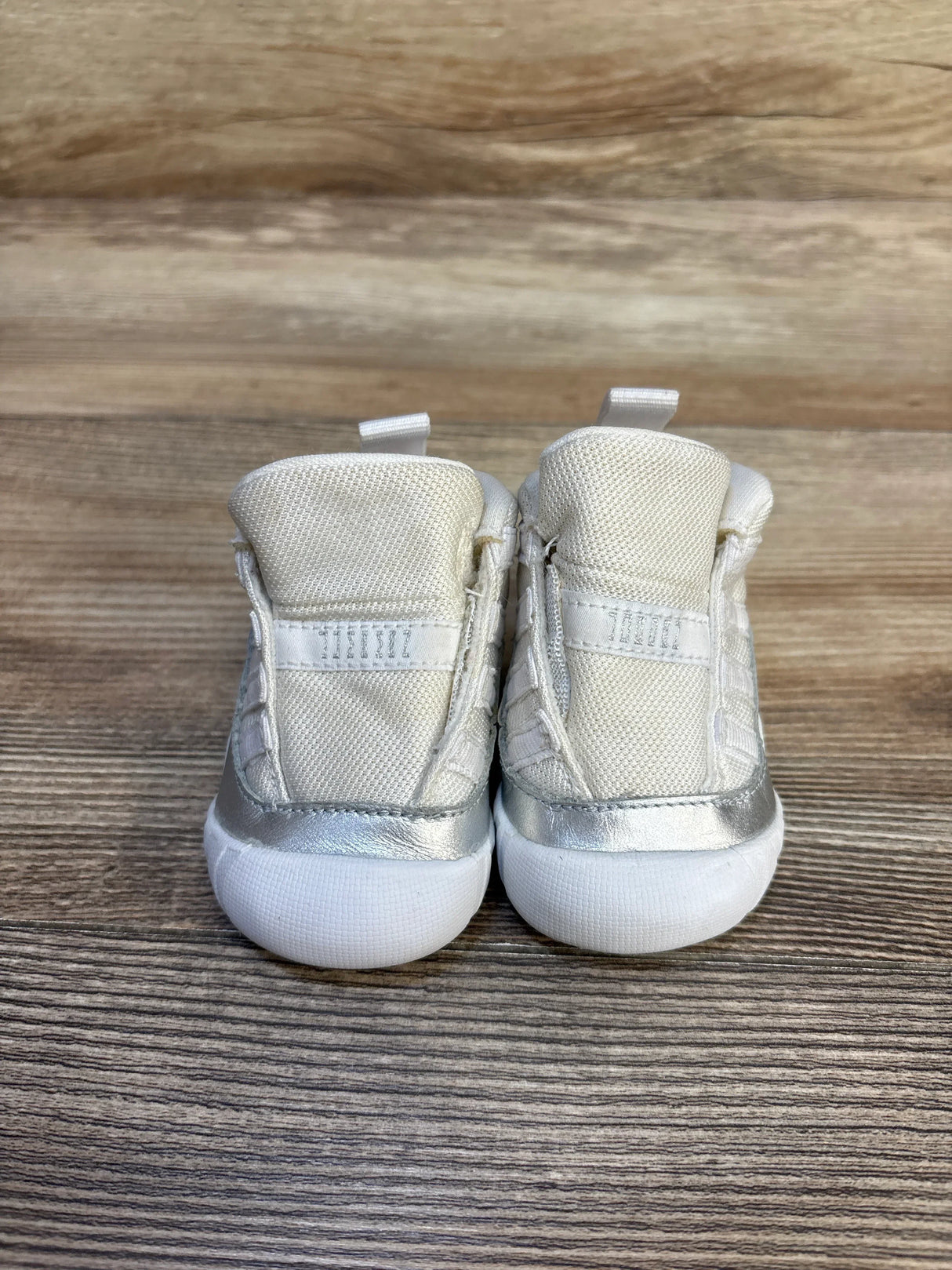 Rear view of Air Jordan 11 Retro TD Metallic Silver sneakers size 2C with metallic silver trim and white rubber soles on wood background