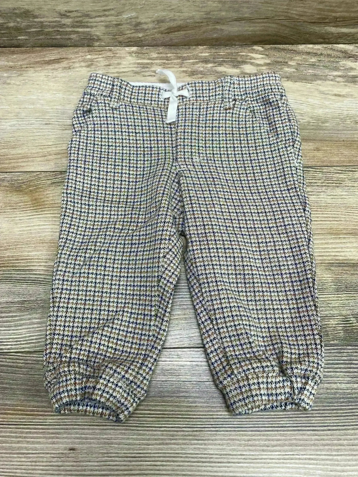 Flat lay of houndstooth baby jogger pants showing brown pattern, white drawstring and elastic cuffs on light wood background